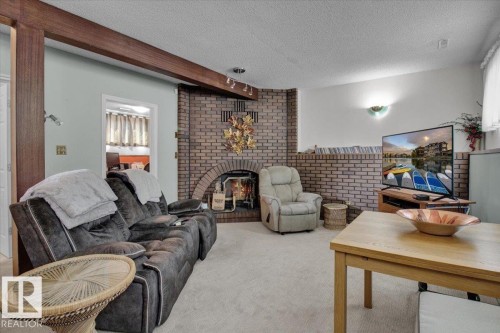 Living area featuring carpeted flooring, a brick fireplace, and a textured ceiling - 3523 18A Avenue, Edmonton, AB - Indoor Photo Showing Living Room With Fireplace