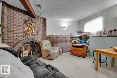 Living area featuring a brick fireplace, a wood ceiling beam, and a large window with white curtains - 3523 18A Avenue, Edmonton, AB - Indoor With Fireplace