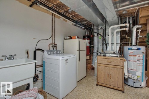 The utility area includes a white utility sink with a chrome faucet, a white washing machine, and a water heater - 3523 18A Avenue, Edmonton, AB - Indoor Photo Showing Laundry Room