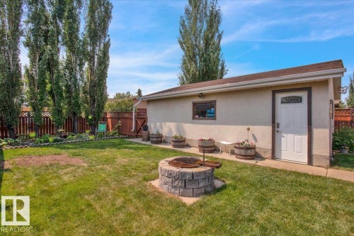 The property features an extensive backyard with a well-maintained lawn and a stone-built fire pit - 3523 18A Avenue, Edmonton, AB - Outdoor