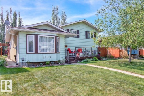 The property features a well-maintained lawn, a paved walkway, and a spacious deck with railing - 3523 18A Avenue, Edmonton, AB - Outdoor