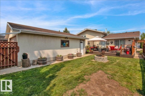 The property features a spacious backyard with a lawn, a stone fire pit, and a wooden deck - 3523 18A Avenue, Edmonton, AB - Outdoor With Deck Patio Veranda