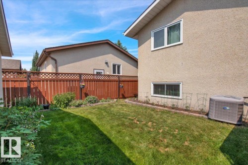 The property features a fenced yard with a lawn, garden beds, and an air conditioning unit visible on the exterior - 3523 18A Avenue, Edmonton, AB - Outdoor With Exterior