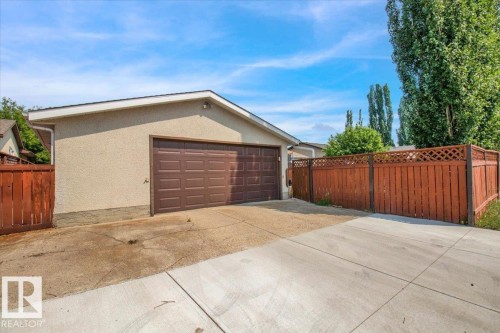 The property features an attached garage with a brown panel door, a paved driveway, and a wooden fence - 3523 18A Avenue, Edmonton, AB - Outdoor With Exterior