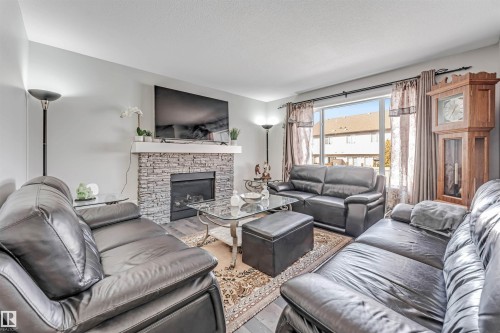 The living room features a fireplace with a stone surround and a white mantel, along with light grey walls and hardwood style flooring - 2244 21 Avenue, Edmonton, AB - Indoor Photo Showing Living Room With Fireplace