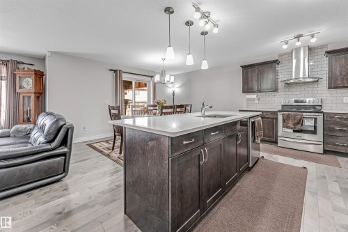 Open concept living area featuring light-toned flooring, a kitchen island with a sink, dark wood cabinetry, and stainless steel appliances - 2244 21 Avenue, Edmonton, AB - Indoor Photo Showing Kitchen With Upgraded Kitchen