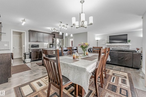 Open concept living space featuring a dining area with a chandelier, a kitchen with dark cabinetry and white subway tile backsplash, and a living room with a stone-faced fireplace - 2244 21 Avenue, Edmonton, AB - Indoor Photo Showing Dining Room
