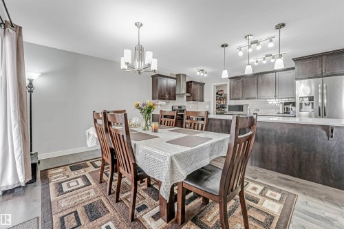 The dining area features a chandelier and wood flooring, opening to a kitchen with dark cabinetry, stainless steel appliances, and a white subway tile backsplash - 2244 21 Avenue, Edmonton, AB - Indoor Photo Showing Dining Room