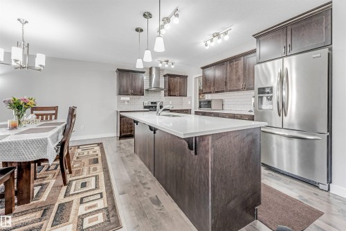 The kitchen and dining area feature light-toned flooring, an expansive kitchen island with a white countertop, and dark wood cabinetry - 2244 21 Avenue, Edmonton, AB - Indoor Photo Showing Other Room