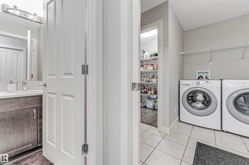 This practical space includes a laundry area with two front-loading washing machines, a wired shelving unit, and tiled flooring - 2244 21 Avenue, Edmonton, AB - Indoor Photo Showing Laundry Room