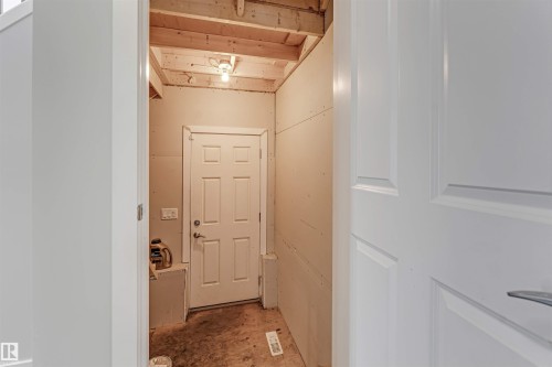 Interior space featuring a white paneled door, exposed ceiling joists, and a single light fixture - 2244 21 Avenue, Edmonton, AB - Indoor Photo Showing Other Room