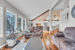 The property features an inviting living area with hardwood flooring, a vaulted ceiling with exposed beams, and a wall of windows providing natural light - 