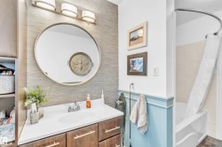 Bathroom vanity with a white countertop and dark wood cabinetry, featuring a large round mirror and overhead lighting - 