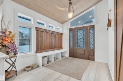 Welcoming entryway featuring a decorative wood front door with sidelights, a custom wood slat bench with coat hooks, and large windows providing natural light - 