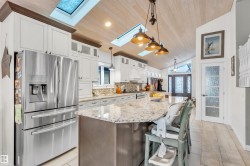 The kitchen features white cabinetry, a large kitchen island with a granite countertop, and a vaulted ceiling with skylights and recessed lighting - 
