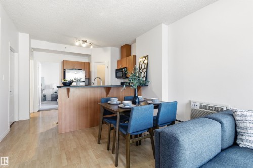 Open concept living area featuring hardwood flooring, a kitchen with wood cabinetry and stainless steel appliances, and a dining area - 601 10504 99 Avenue, Edmonton, AB - Indoor