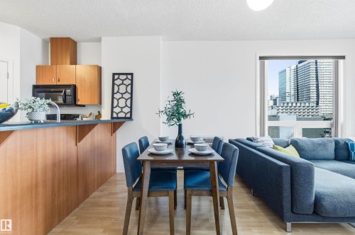The open-concept living area features light wood flooring, a kitchen with wood cabinetry and black appliances, and a dining area with a modern table and chairs - 601 10504 99 Avenue, Edmonton, AB - Indoor