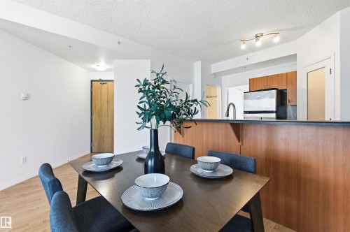 The dining area features light-toned flooring, a dark-toned dining table, and a partial view of the kitchen with wood cabinetry and stainless steel appliances - 601 10504 99 Avenue, Edmonton, AB - Indoor Photo Showing Dining Room