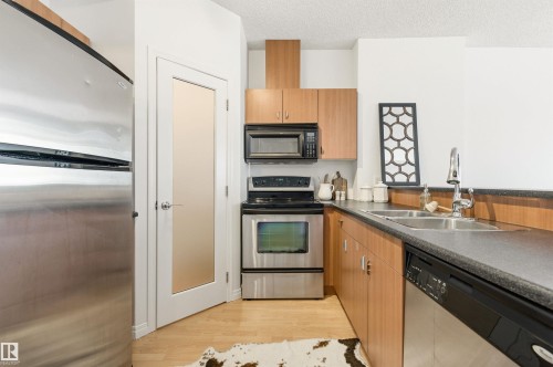 The kitchen features hardwood floors, light-toned cabinetry, stainless steel appliances, and a double basin sink - 601 10504 99 Avenue, Edmonton, AB - Indoor Photo Showing Kitchen With Double Sink