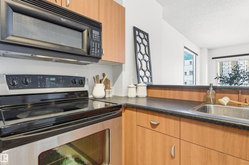 The kitchen features wood cabinetry, dark countertops, a stainless steel oven with a black cooktop, and an overhead microwave - 601 10504 99 Avenue, Edmonton, AB - Indoor Photo Showing Kitchen