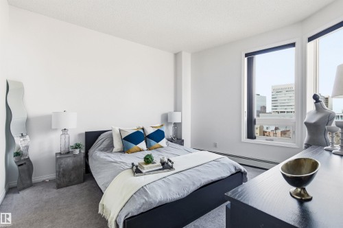 This inviting room features soft grey carpeting, bright white walls, and a large window offering urban views - 601 10504 99 Avenue, Edmonton, AB - Indoor Photo Showing Bedroom