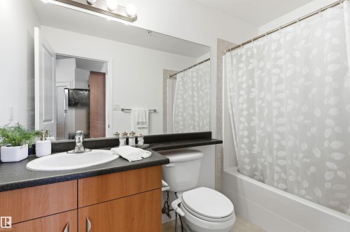Bathroom featuring a wooden vanity with a dark countertop, an oval sink with a chrome faucet, and a bathtub with a white shower curtain - 601 10504 99 Avenue, Edmonton, AB - Indoor Photo Showing Bathroom