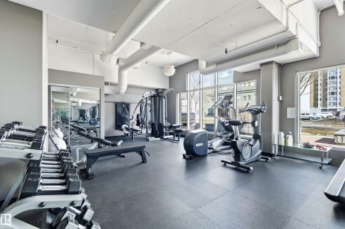 Fitness room featuring a selection of exercise equipment, large windows providing natural light, and a mirrored wall - 601 10504 99 Avenue, Edmonton, AB - Indoor Photo Showing Gym Room