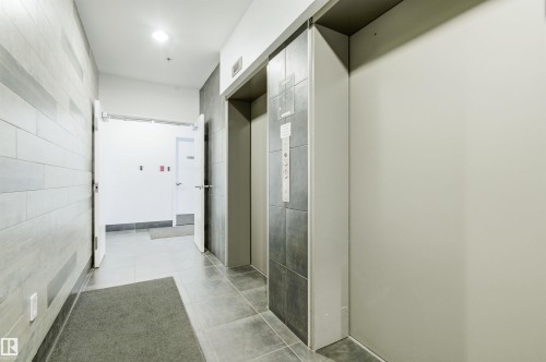 The property features a hallway with light-toned tiled walls and flooring, leading towards an open doorway - 601 10504 99 Avenue, Edmonton, AB - Indoor Photo Showing Other Room