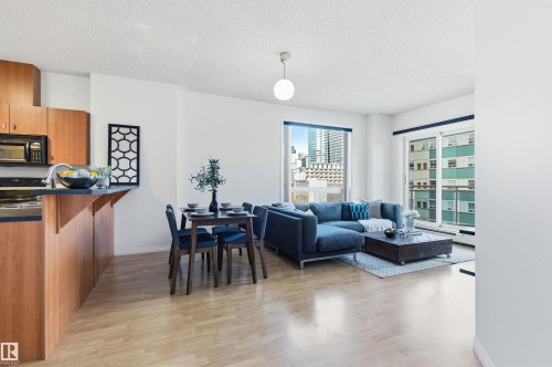 This open-concept living area features light wood flooring, large windows, and a kitchen with wood cabinetry and black countertops - 601 10504 99 Avenue, Edmonton, AB - Indoor