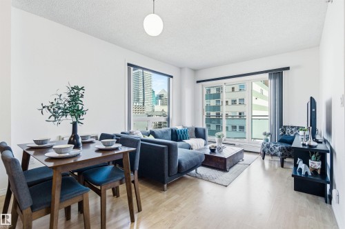This bright living area features light wood flooring, white walls, and a large window offering urban views - 601 10504 99 Avenue, Edmonton, AB - Indoor