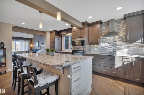 Modern kitchen featuring hardwood floors, a large center island with a light-colored countertop, and stainless steel appliances including a wall oven and range hood - 8807 31 Avenue, Edmonton, AB - Indoor Photo Showing Kitchen With Upgraded Kitchen