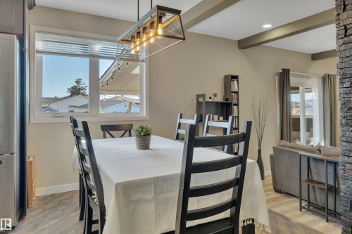 Dining area featuring a modern chandelier, a window with blinds, and durable flooring, with views into an adjacent living space - 8807 31 Avenue, Edmonton, AB - Indoor Photo Showing Dining Room