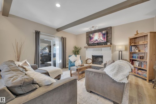 Living area featuring a white brick fireplace with a stone facade, wood flooring, and recessed lighting - 8807 31 Avenue, Edmonton, AB - Indoor Photo Showing Other Room With Fireplace