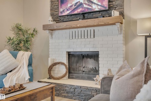 The living area features a white brick fireplace with a stone hearth and a wooden mantel - 8807 31 Avenue, Edmonton, AB - Indoor With Fireplace