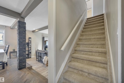 The property features a staircase with carpeted treads and a white handrail, alongside a room with wood-style flooring and a decorative stone column - 8807 31 Avenue, Edmonton, AB - Indoor Photo Showing Other Room