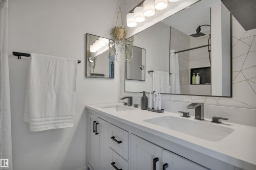 Bathroom featuring a dual vanity with white countertops, black matte fixtures, and a large mirror with integrated lighting - 8807 31 Avenue, Edmonton, AB - Indoor Photo Showing Bathroom