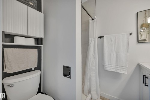 Bathroom featuring a white toilet, white cabinets with textured doors, and a shower with a white curtain - 8807 31 Avenue, Edmonton, AB - Indoor Photo Showing Bathroom
