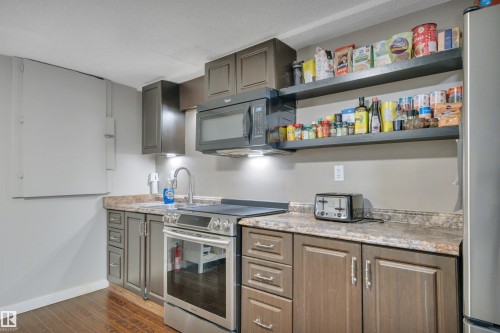 The kitchen features dark wood cabinetry, a stainless steel oven with a range, and a microwave - 8807 31 Avenue, Edmonton, AB - Indoor Photo Showing Kitchen