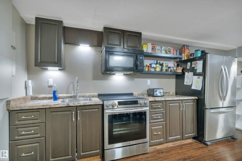 The kitchen features dark cabinetry, granite-style countertops, and stainless steel appliances including a refrigerator, stove, and microwave - 8807 31 Avenue, Edmonton, AB - Indoor Photo Showing Kitchen With Upgraded Kitchen