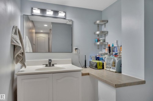 Bathroom featuring a vanity with a white countertop and sink, a vanity mirror with overhead lighting, and a wall-mounted shelving unit - 8807 31 Avenue, Edmonton, AB - Indoor Photo Showing Other Room