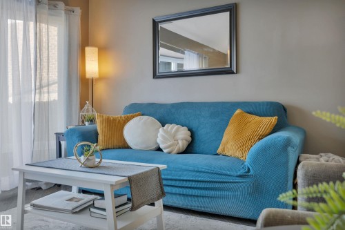 This inviting living area features neutral-toned walls, a large window with sheer white curtains, and a floor lamp providing ambient lighting - 8807 31 Avenue, Edmonton, AB - Indoor