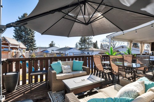The property features an extensive deck with outdoor seating, a large patio umbrella, and a covered section with string lights - 8807 31 Avenue, Edmonton, AB - Outdoor With Deck Patio Veranda With Exterior