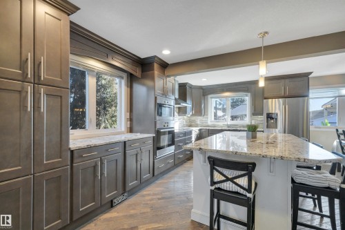 The kitchen features extensive cabinetry, a large kitchen island with a stone countertop, built-in stainless steel appliances, and hardwood floors - 8807 31 Avenue, Edmonton, AB - Indoor Photo Showing Kitchen With Upgraded Kitchen