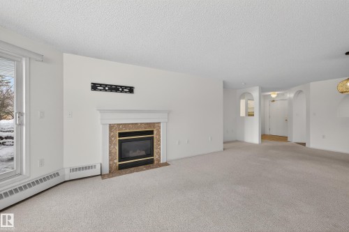 Living room featuring a fireplace with a stone surround, light-colored carpeting, and a sliding glass door providing natural light - 106 15499 Castle Downs Road, Edmonton, AB - Indoor Photo Showing Living Room With Fireplace