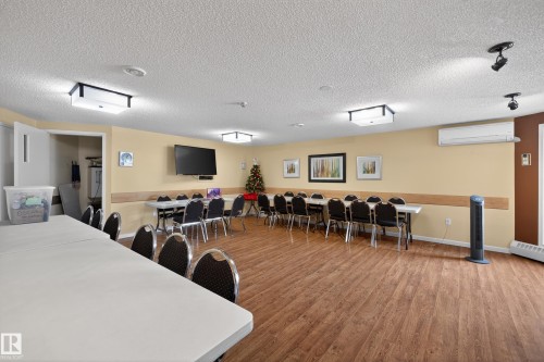 Spacious common room featuring wood-look flooring, ample overhead lighting, wall-mounted television, and several tables and chairs - 106 15499 Castle Downs Road, Edmonton, AB - Indoor Photo Showing Other Room