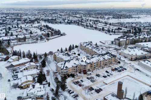 This property features a multi-story building with a light-colored facade and dark roofs, situated near a large frozen body of water - 106 15499 Castle Downs Road, Edmonton, AB - Outdoor With View