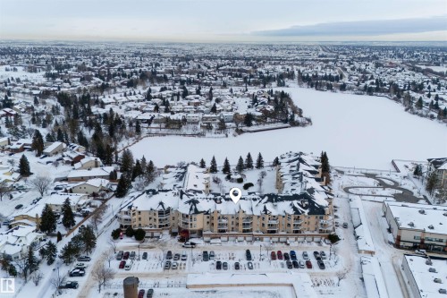 Aerial view of the property, featuring a multi-story building with a snow-covered roof, situated across from a frozen lake - 106 15499 Castle Downs Road, Edmonton, AB - Outdoor With View