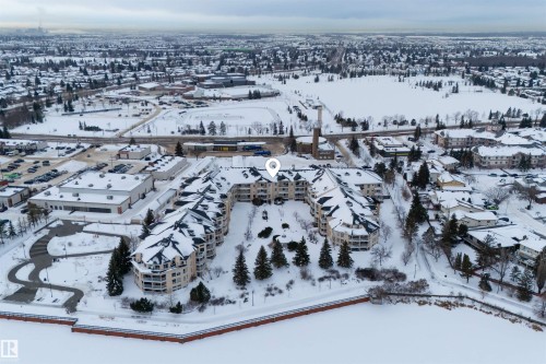 Aerial view of the property and its surrounding area, featuring a multi-story building with snow-covered roofs and balconies, located adjacent to a snow-covered body of water - 106 15499 Castle Downs Road, Edmonton, AB - Outdoor With View