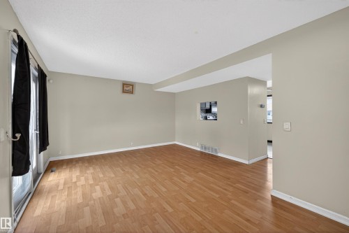 Living room featuring light wood flooring, neutral tone walls, and a large window with vertical blinds - 3301 139 Avenue, Edmonton, AB - Indoor Photo Showing Other Room