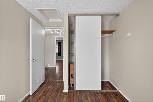 This room features rich wood-look flooring, neutral wall tones, and a closet with sliding doors and an integrated shelving unit - 3301 139 Avenue, Edmonton, AB - Indoor Photo Showing Other Room
